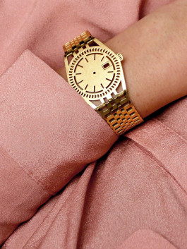 Golden TIMEPEACE bracelet worn on the wrist, watch-inspired jewelry symbolizing mindfulness and living in the present moment, styled with a pink blouse 