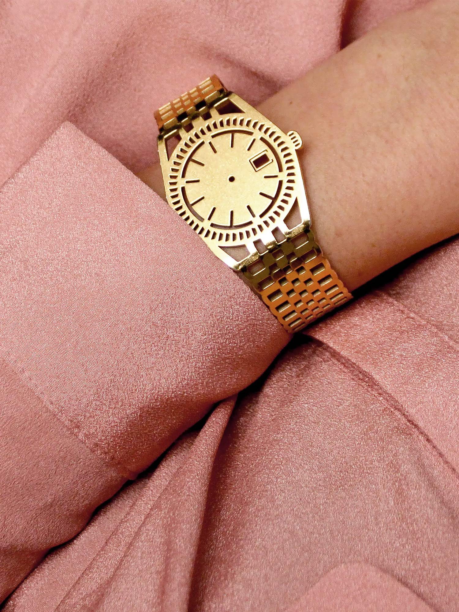 Golden TIMEPEACE bracelet worn on the wrist, watch-inspired jewelry symbolizing mindfulness and living in the present moment, styled with a pink blouse