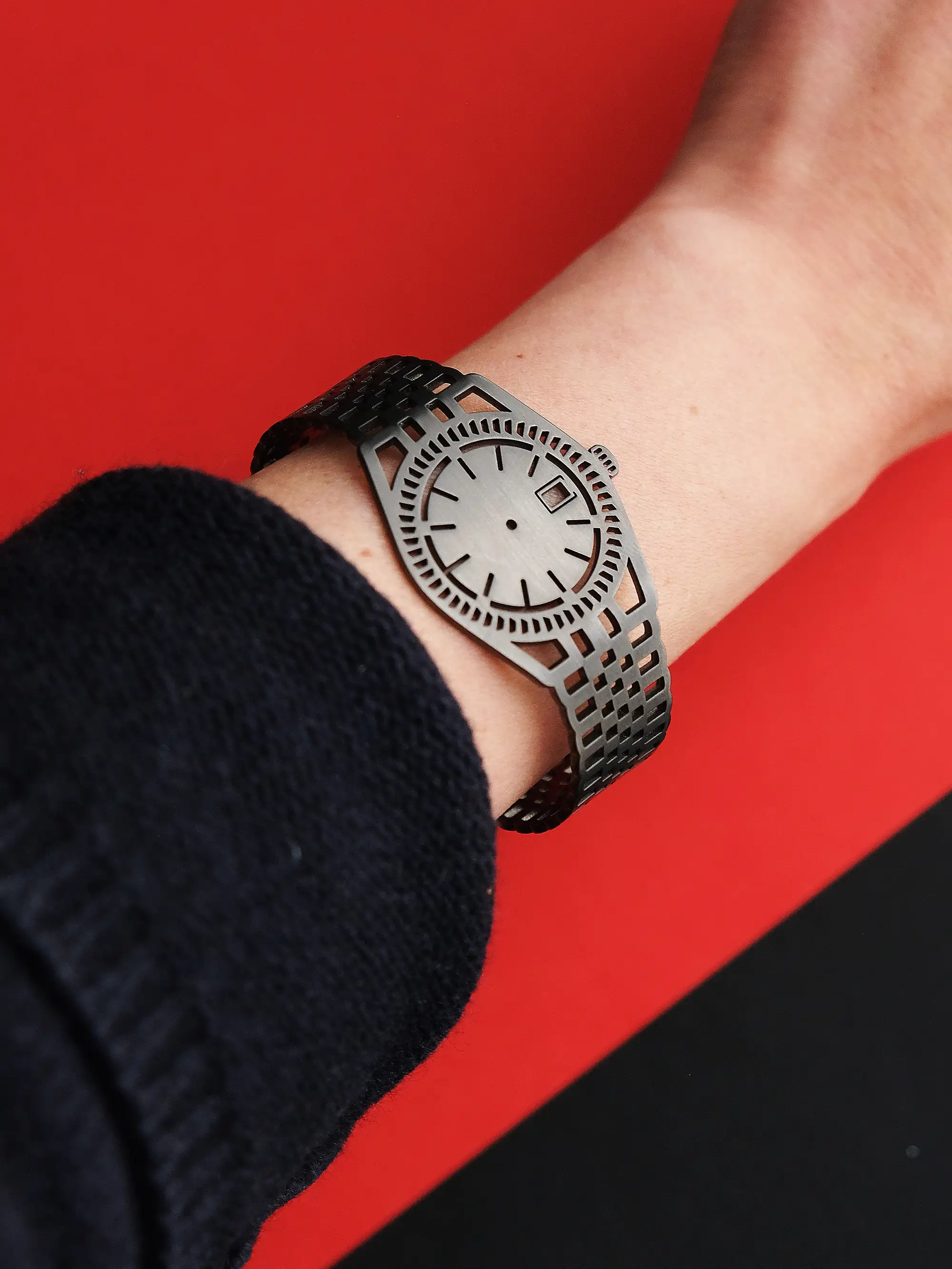 TIMEPEACE bracelet worn on wrist, with a dark grey finish, as a symbol of mindfulness and living in the present moment, photographed on a red background