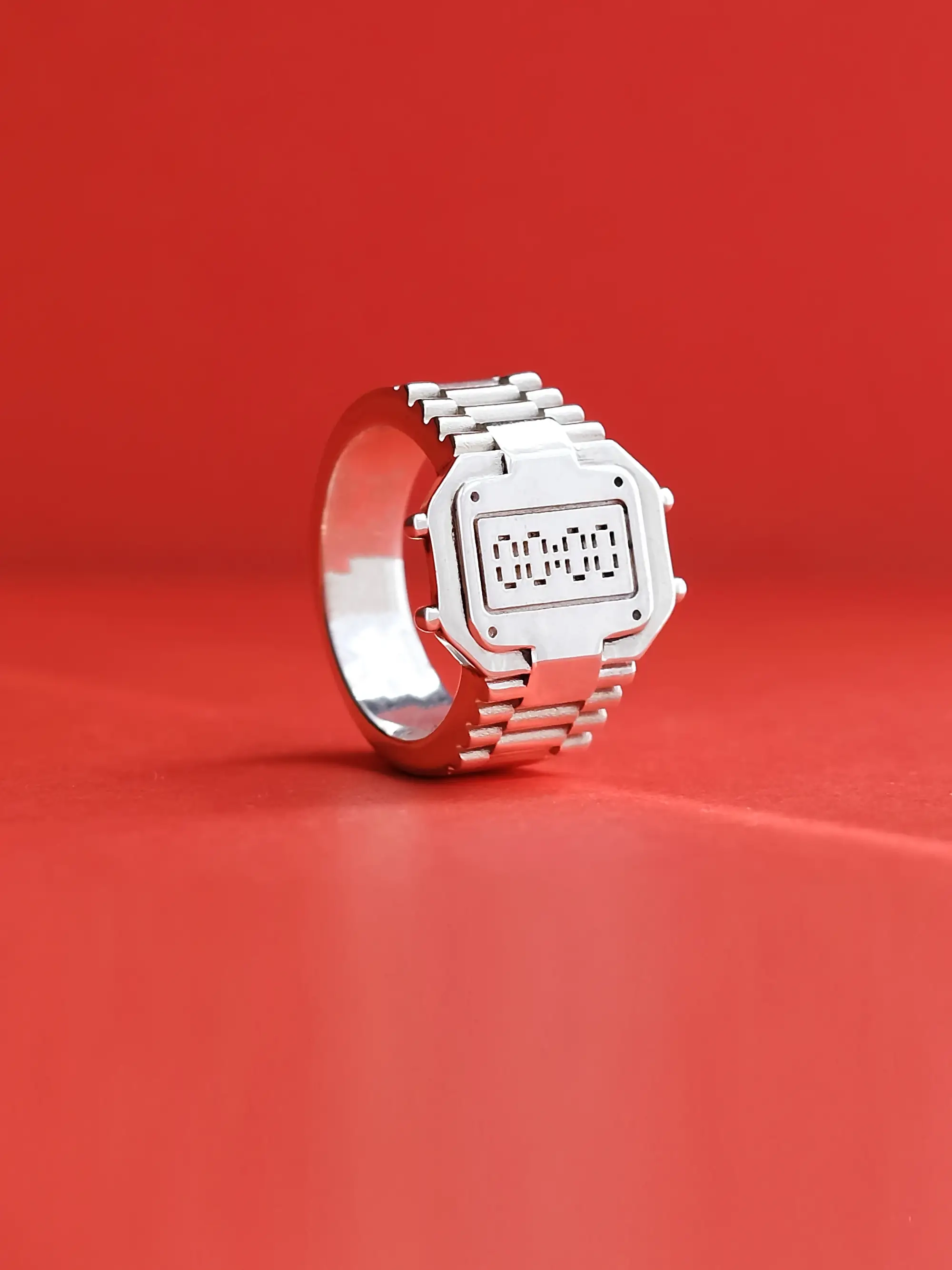 TIMEPEACE casio-style watch ring in recycled 925 sterling silver, clock-inspired ring design without showing time, front view on red background