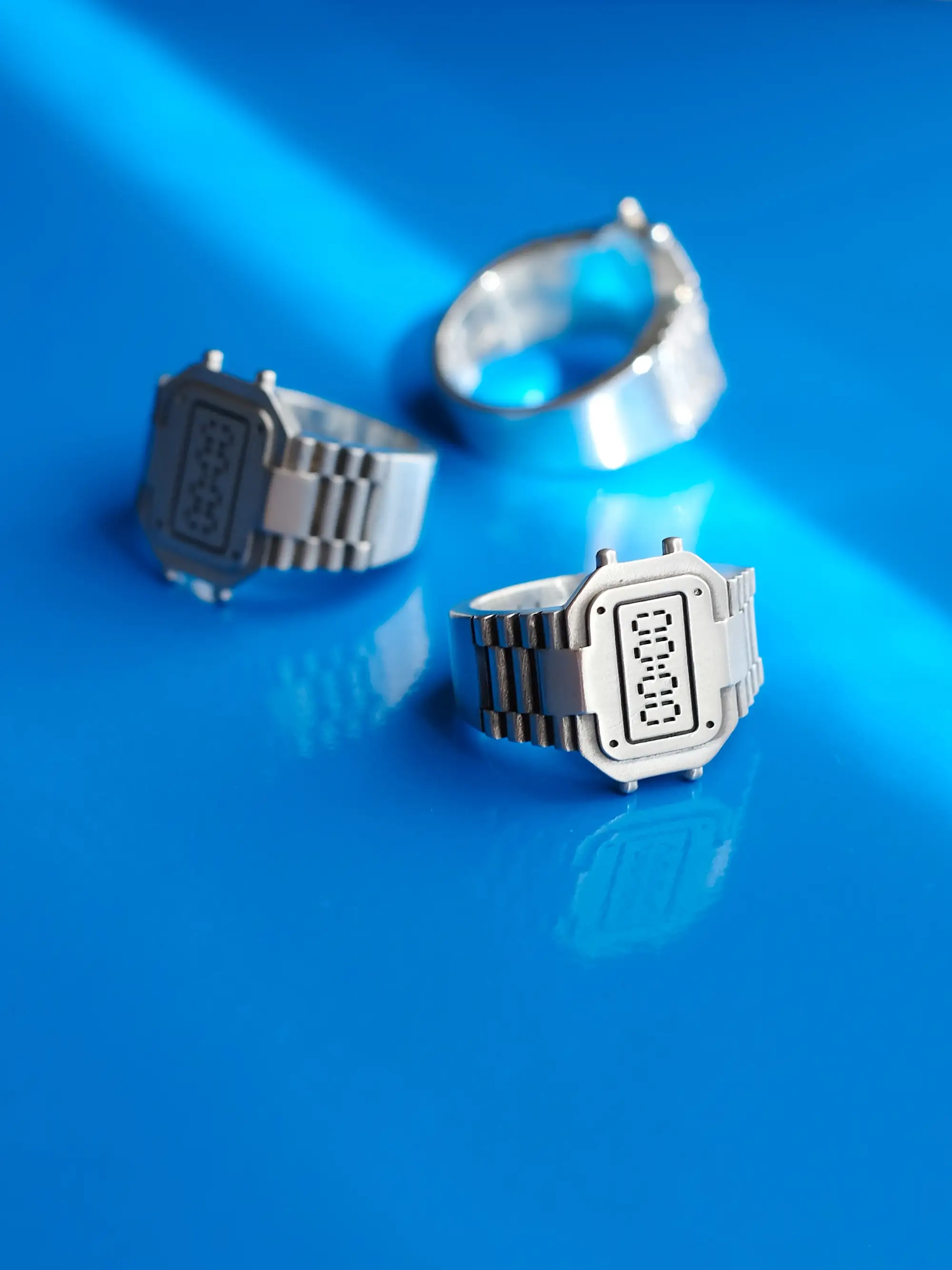 TIMEPEACE watch-inspired rings worn as modern jewelry, recycled sterling silver clockring representing restart and reset, lying on blue background