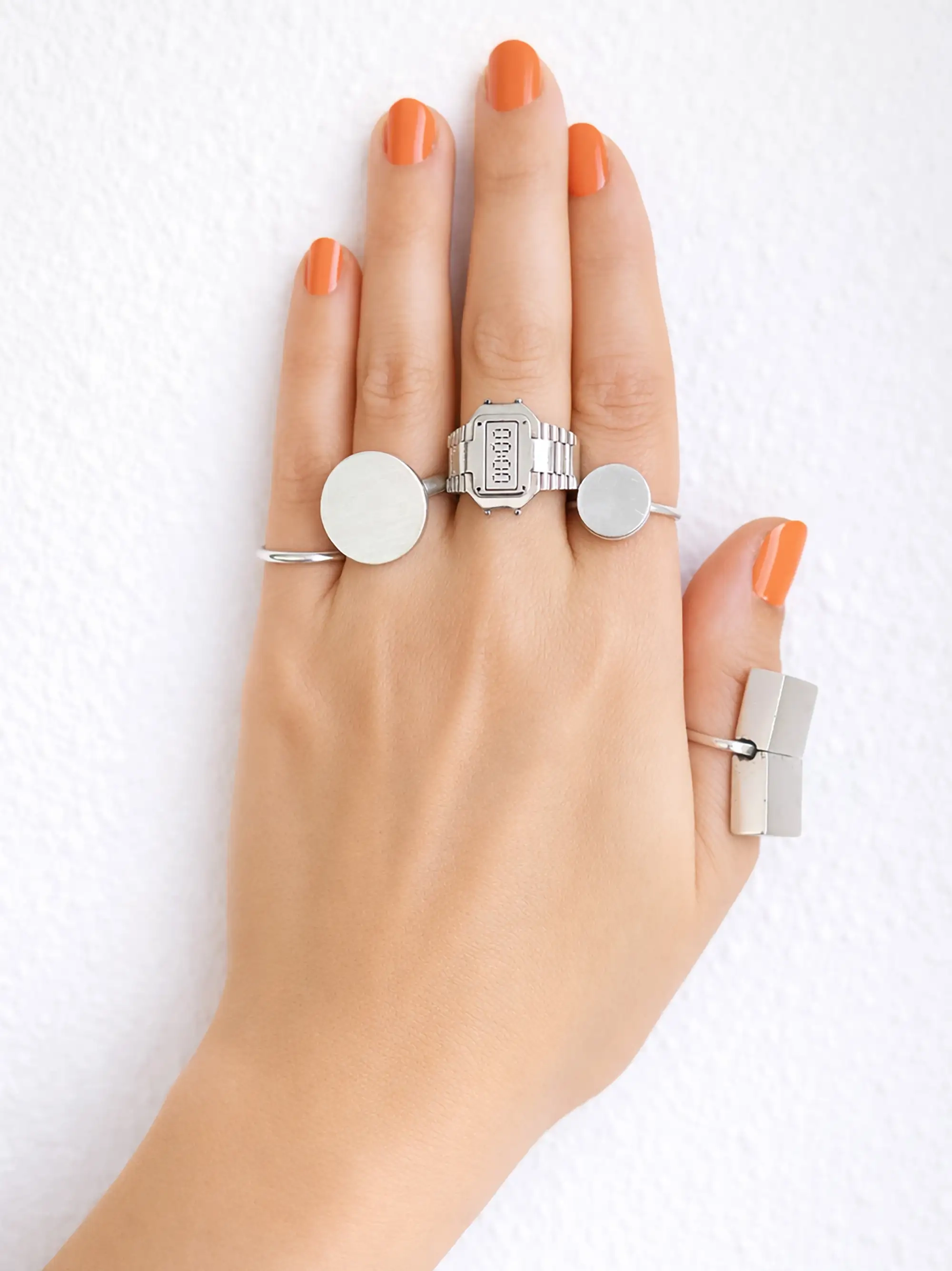 Hand with orange nails wearing a TIMEPEACE watch ring, two round SUN ring, one MEMORY BOX ring, recycled sterling silver ringwatch inspired by digital watches, minimalist design jewelry with concept